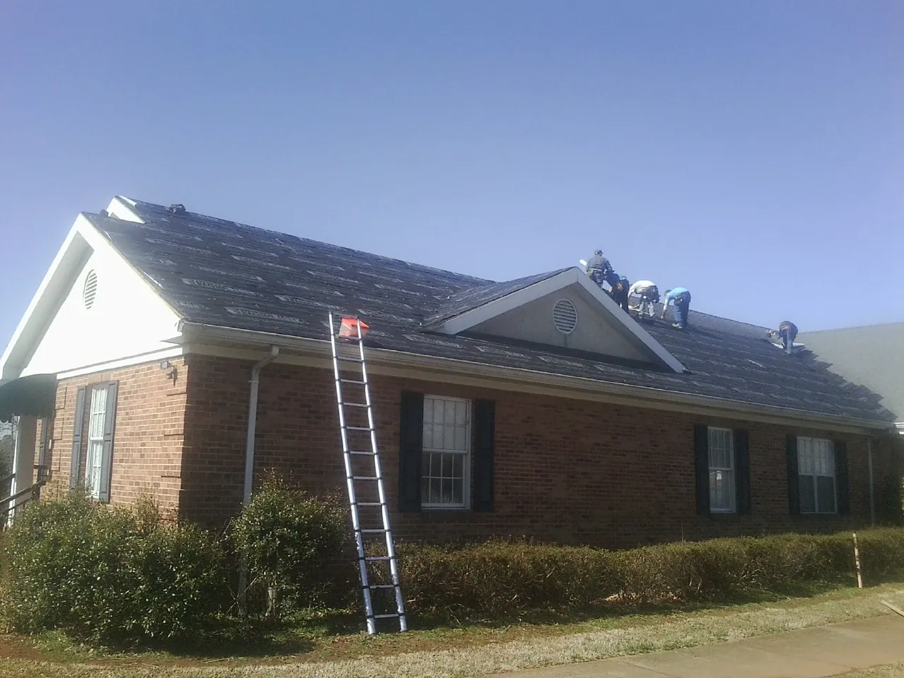 Crew tearing shingles off a brick ranch roof with a ladder set — Emergency Roof Repair work by our crew in Bonsall