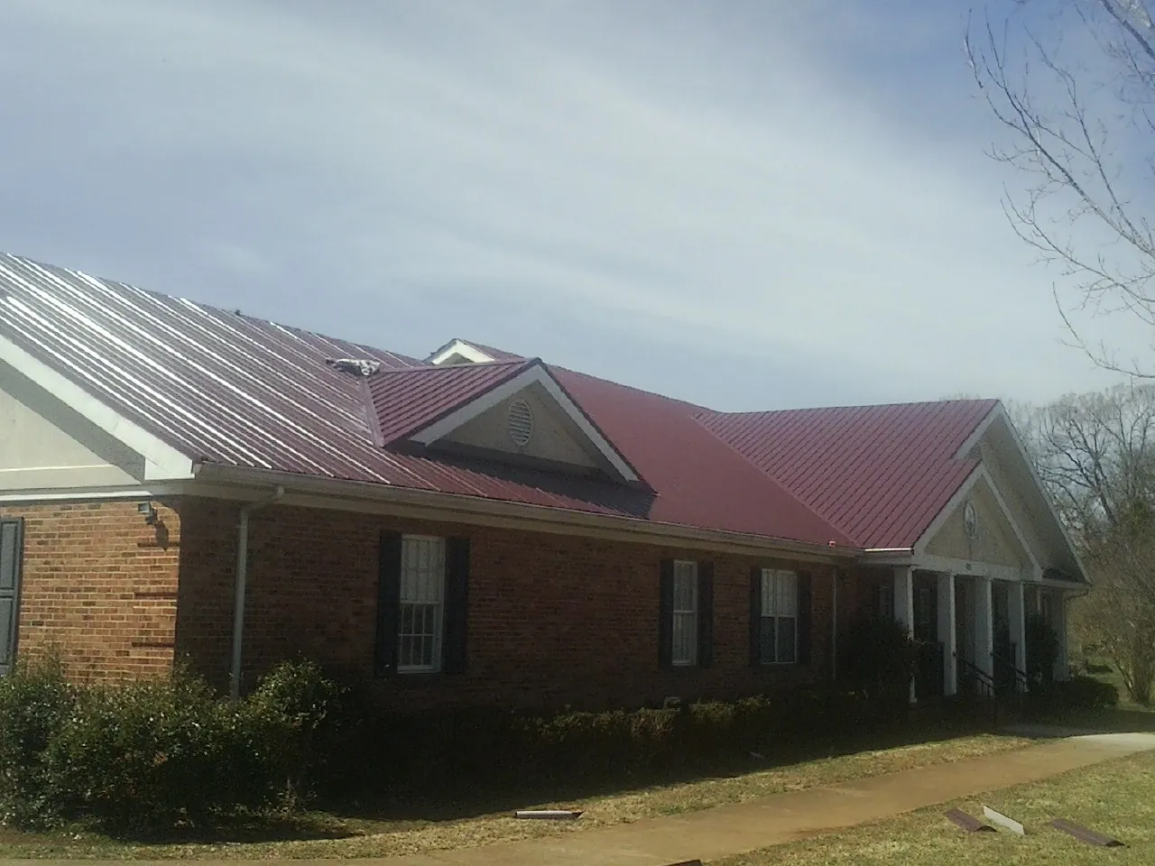 Red metal roof with gabled entries on a long brick building, from a Hail Damage Roof Repair job in Bonsall