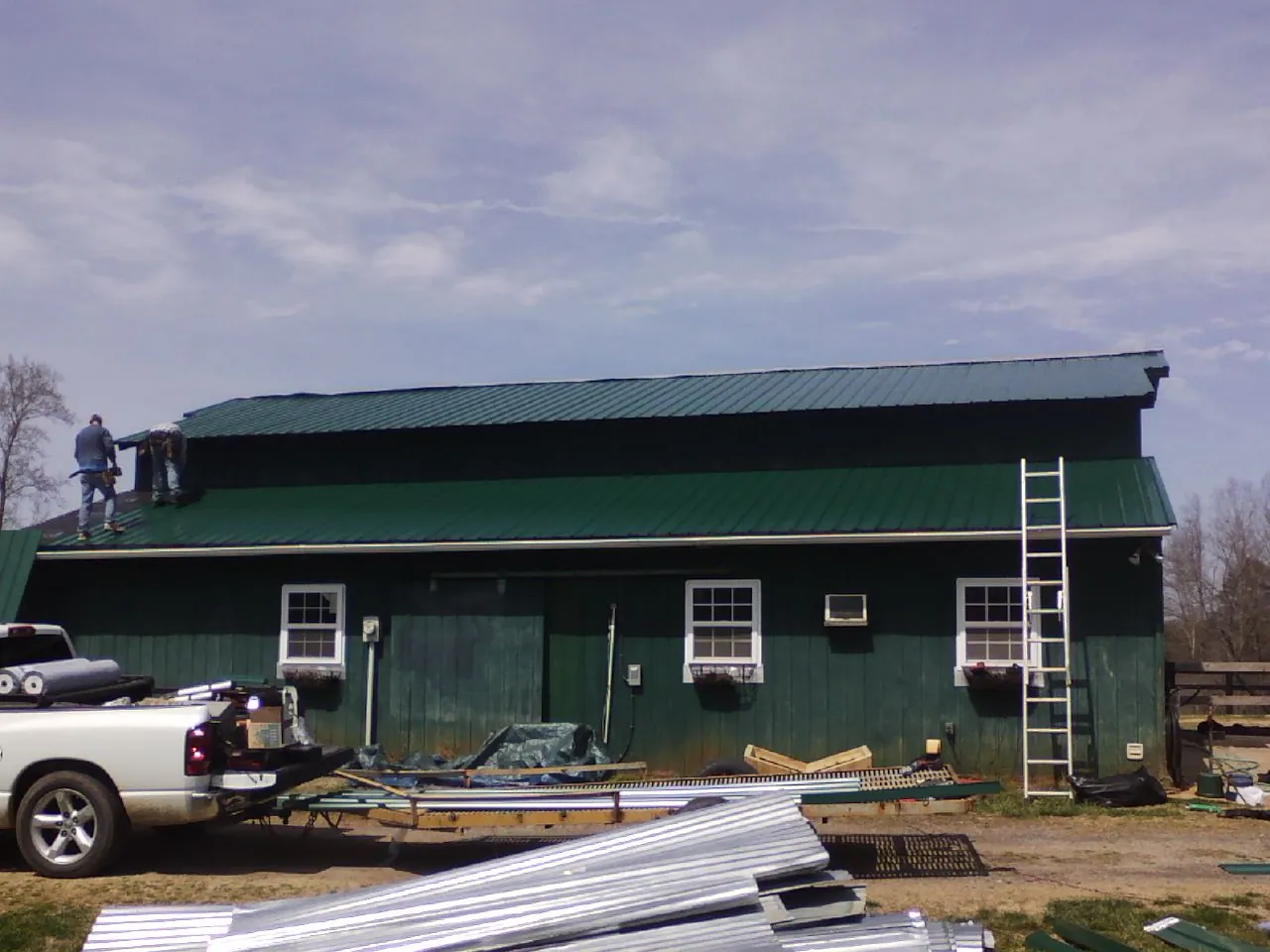 Crew installing green metal roofing on a large green barn in Bonsall