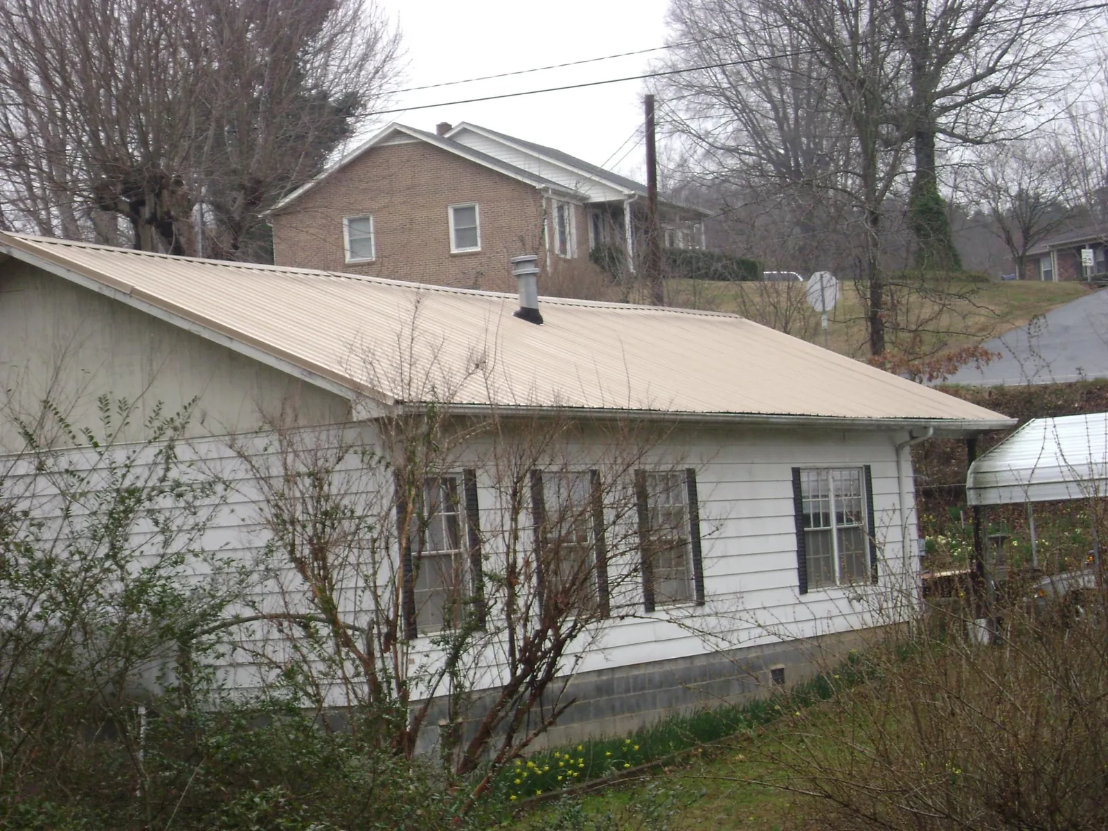 Tan metal roof on a white sided house set into a hillside — Commercial Roofing by Roofing Brothers in Bonsall